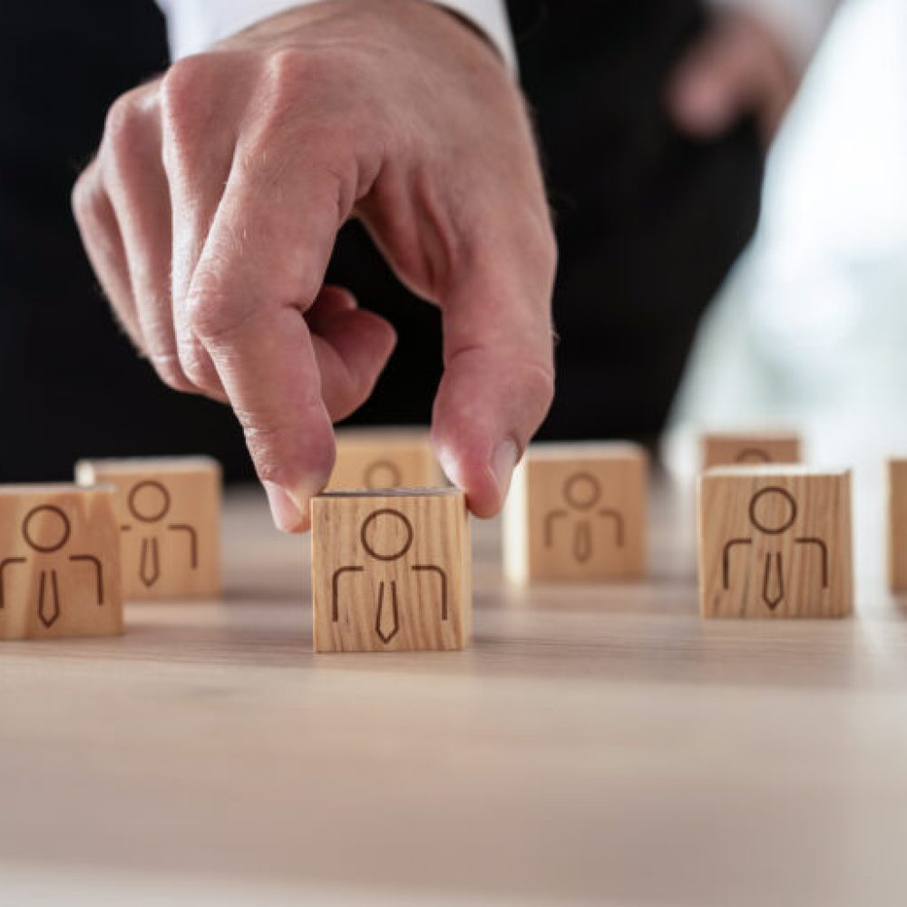 Human resources concept - businessman arranging wooden cubes with people icon on office desk.